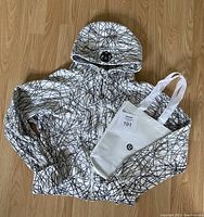 Full view of Lululemon Scuba Hoodie and white tote bag laid flat on wooden floor.