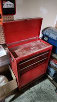 Red rolling tool box closed showing lift-top lid, three drawers, and bottom cabinet door closed with some surface dirt.