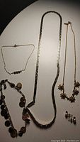 Overall view of all jewelry items laid out, showing two necklaces, a bracelet with disc charms, a pair of pearl and sapphire stud earrings, and a gold anklet chain.
