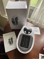 Photo of the plug-in heater with its box and instruction manual on wooden surface near window.