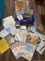 Wide view of all stationery items including cards, journals, envelopes, sticky notes, calendar memo pads, pens and memory card inside blue bin container on floor