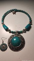 Photo of vintage turquoise-colored bracelet with large circular pendant and beads, and matching earrings with turquoise stones arranged in round floral patterns