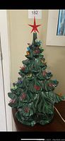 Front view of vintage ceramic Christmas tree showing green color, multiple colorful bulb covers and red star topper.