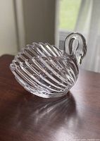 Clear lead crystal swan candy dish with ribbed body and curved neck and head, displayed on wooden surface by window.