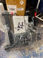 Bike trainer stand in black metal frame with a red lever, concerted with packaging and manual in a plastic bag.