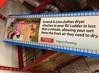 Boxed Extend-A-Line clothes dryer showing promotional image and usage instructions attached to an RV ladder.