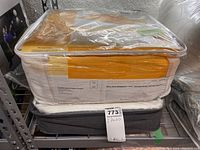 Queen white goose down duvet and twin down comforter packaged and stacked on a metal shelving unit.