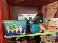 Overview of electronic items in the lot, including boxed TP-Link Kasa smart bulbs, Flarecon Air 2 transmitter box, and other assorted boxes.