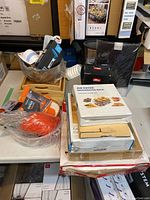 General photo showing a variety of kitchen items including trays, racks, bowls, and packaged kitchen gadgets grouped on a table.