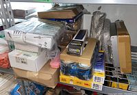 Shelf containing stacked unopened boxes of office supplies including labels, badge holders, and plastic sleeves