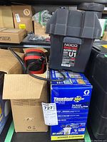 Photo showing NOCO Snap-Top U1 battery box, Graco TrueCoat 360 DS paint sprayer box, and other items in storage area.