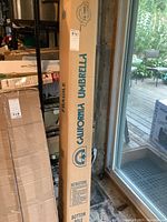 Tall cardboard box labeled California Umbrella, storing the patio umbrella in original packaging