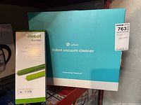 Blue Lefant robot vacuum cleaner box from another angle alongside a tall box of green iRobot rubber brushes for Roomba.