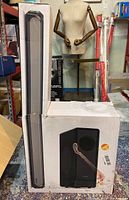 Photo showing the boxed soundbar and subwoofer unit at warehouse with mannequin and some inventory in the background.