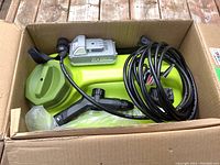 Box containing Sun Joe 24V portable power washer with attached hose, spray gun, and 24V lithium-ion Snow Joe battery pack.