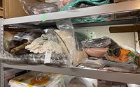 Metal shelving unit holding folded woven and faux fur blankets along with assorted piled pillows in plastic bags.