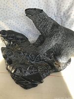 Photo showing side view of black soapstone sculpture of aardvark on a textured base featuring natural elements.