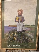 Poster showing Anne of Green Gables standing outdoors with flowers near a water body, framed with gold trim