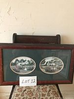 Framed pair of oval prints in a wooden frame with green matting on a patterned chair and wooden background.