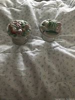 Pair of small porcelain decorative pieces with hand-painted fruit and vegetable designs on cloth background.