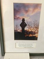 Framed print showing silhouette of Celtic cross at sunset, with bare trees and clouds, and a quote below the image. Gold trim frame visible.