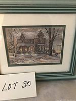 Framed print by Trisha Romance showing a snow-covered house in a winter landscape with trees and a pathway, in a green frame with an inner mat.