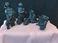 Photo showing front and side view of multiple soapstone Inuit nativity figurines, including standing adults and a baby in a cradle.