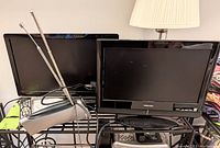 Two 18-inch Toshiba TVs on a metal wire rack, both TVs black, accompanied by two remote controls and a rabbit ear antenna attached to one TV.