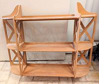 Light wood wall hanging shelves with three tiers, X-shaped side design, no visible damage, intended for wall mounting.