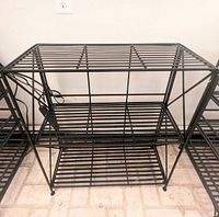 Set of three black metal shelving units shown side by side on floor with pale tile.