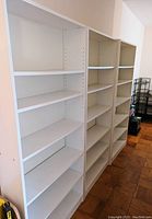 Front and slight side view of three white shelving units showing multiple adjustable shelves and overall height and width.