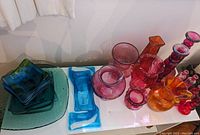 Top view of assorted pink and orange glass vases and blue trays on a white surface