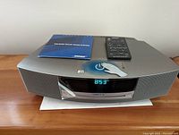 Front-top view of silver Bose Wave Music System with remote and manual on top