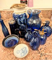 Lot of 13 cobalt blue vases and decorative items on kitchen countertop, including glass and ceramic pieces with one large ceramic pitcher.