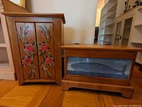 Floral wooden shelf cabinet and wooden whale chest side by side on hardwood floor next to stairs.
