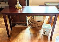 Full view of dark wood foyer table showing rectangular top, four straight legs, wood floor beneath, lamp base on top of the table.