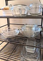 Full view showing multiple clear glass bowls and casserole dishes on metal shelves including clear casserole dishes with lids and white ceramic dish with wooden handle lid