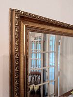 Close-up photo showing detailed carved floral and swirl patterns on the gold frame border of the rectangular mirror.