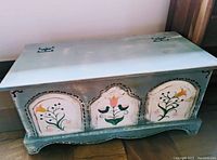 Front and angled view of a wooden hope chest with hand-painted floral designs, showing its size and overall condition.