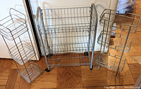 Lot of 3 silver wire storage shelves including one rolling cart and two hanging shelves shown together on floor