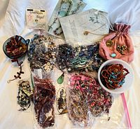 Overview of lot with plastic bags, bowls of beads and jewelry on white background