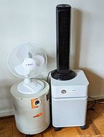 Photo showing the four appliances: small white oscillating fan on top of beige Alter-Air humidifier, black tower fan, and white air purifier with wheels.