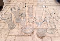 Photo showing the entire set of clear glass and crystal vases and pitchers arranged on the floor, highlighting varying sizes and patterns.
