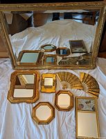 Full view of all mirrors and decorative fans laid on white cloth showing overall lot contents and sizes.