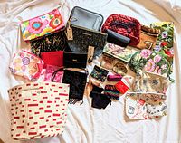 Photo showing the full collection of 28 makeup bags, wallets, and change purses spread out on a white sheet. Items vary in size, color, and material, including floral patterns, quilted textures, and printed zippers.