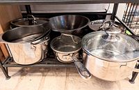 Five stainless steel pots and pans arranged on a shelf showing overall contents of the lot