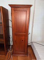 Profile view of the shelving unit showing the wooden paneled door with crown molding top detail.