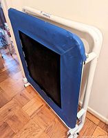 Photo showing the Plyoback rebounder with blue padded edges and black central rebound surface on a white frame against a wall.