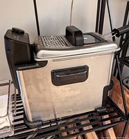 Photo of the T Fal EZ Clean Compact Deep Fryer showing stainless steel body, black control panel with temperature dial, and glass lid with handle.