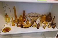 Photo of mustard yellow glass decorative items including bottles, swan-shaped piece, bowls arranged on white shelf